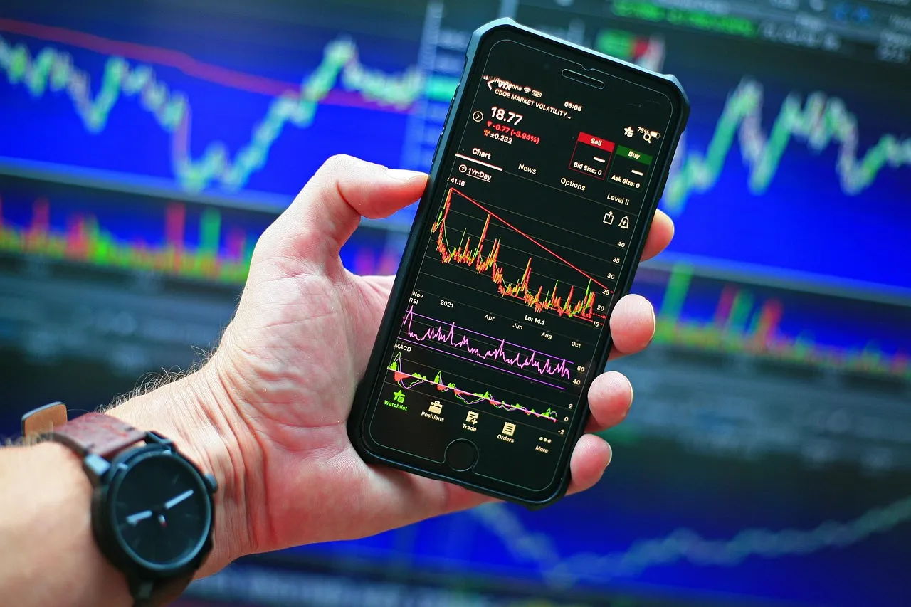 A hand holding a phone showing a stock chart against a wall of market data — illustrating a valuation set without a public market.