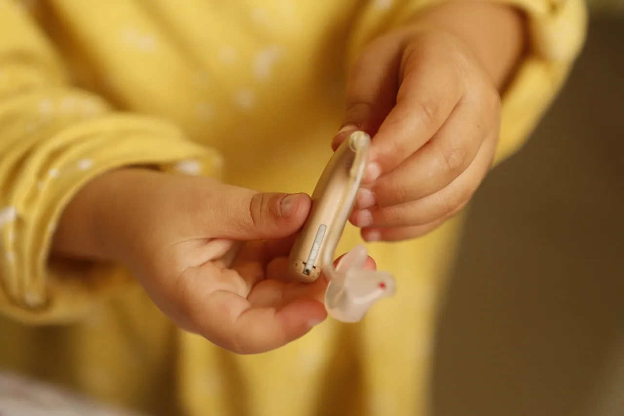 A person's hands holding a small beige behind-the-ear hearing aid