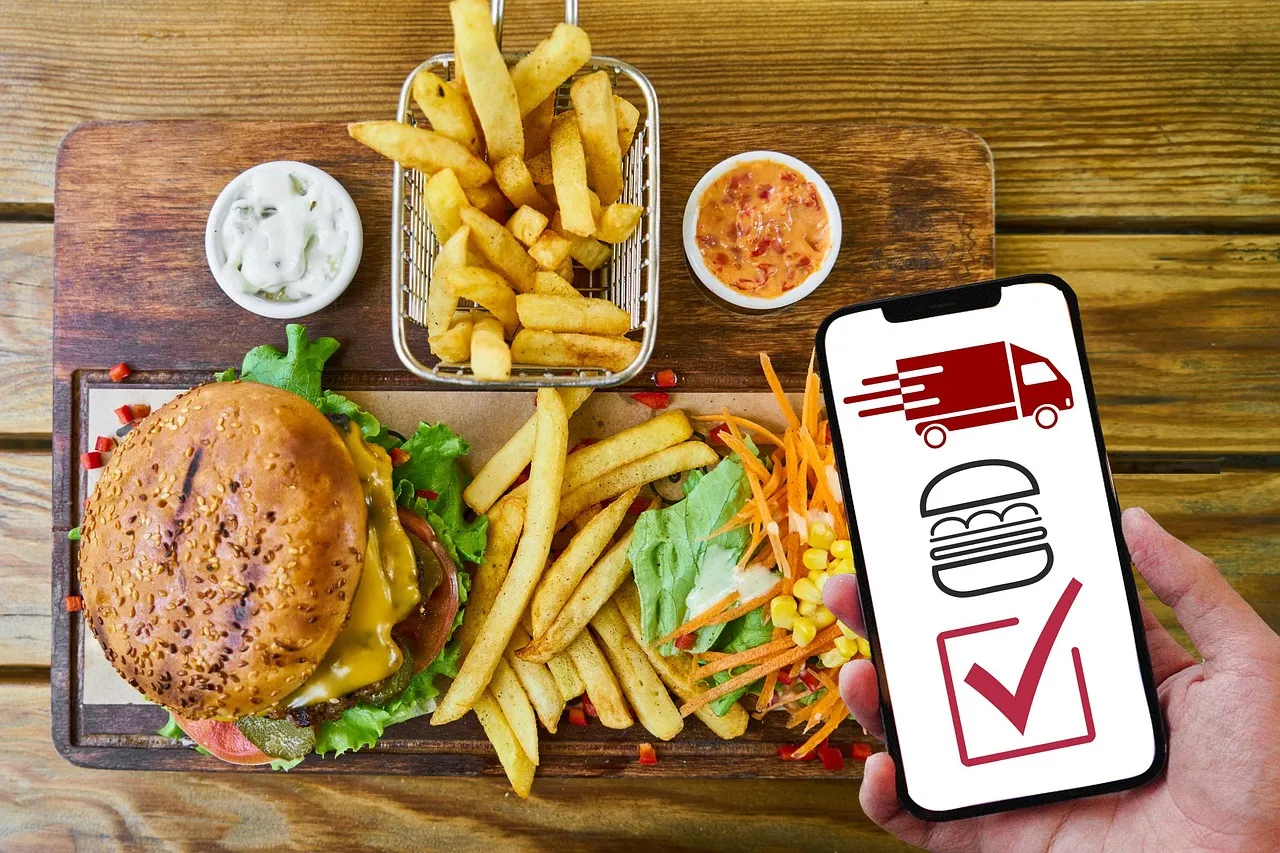A burger and fries beside a smartphone showing a food ordering screen