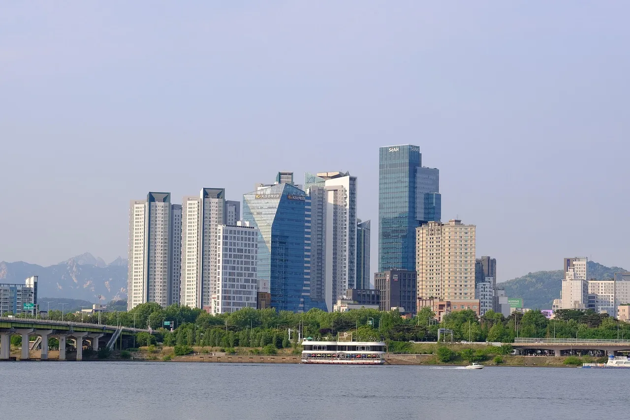 Office towers beside a river, with mountains behind