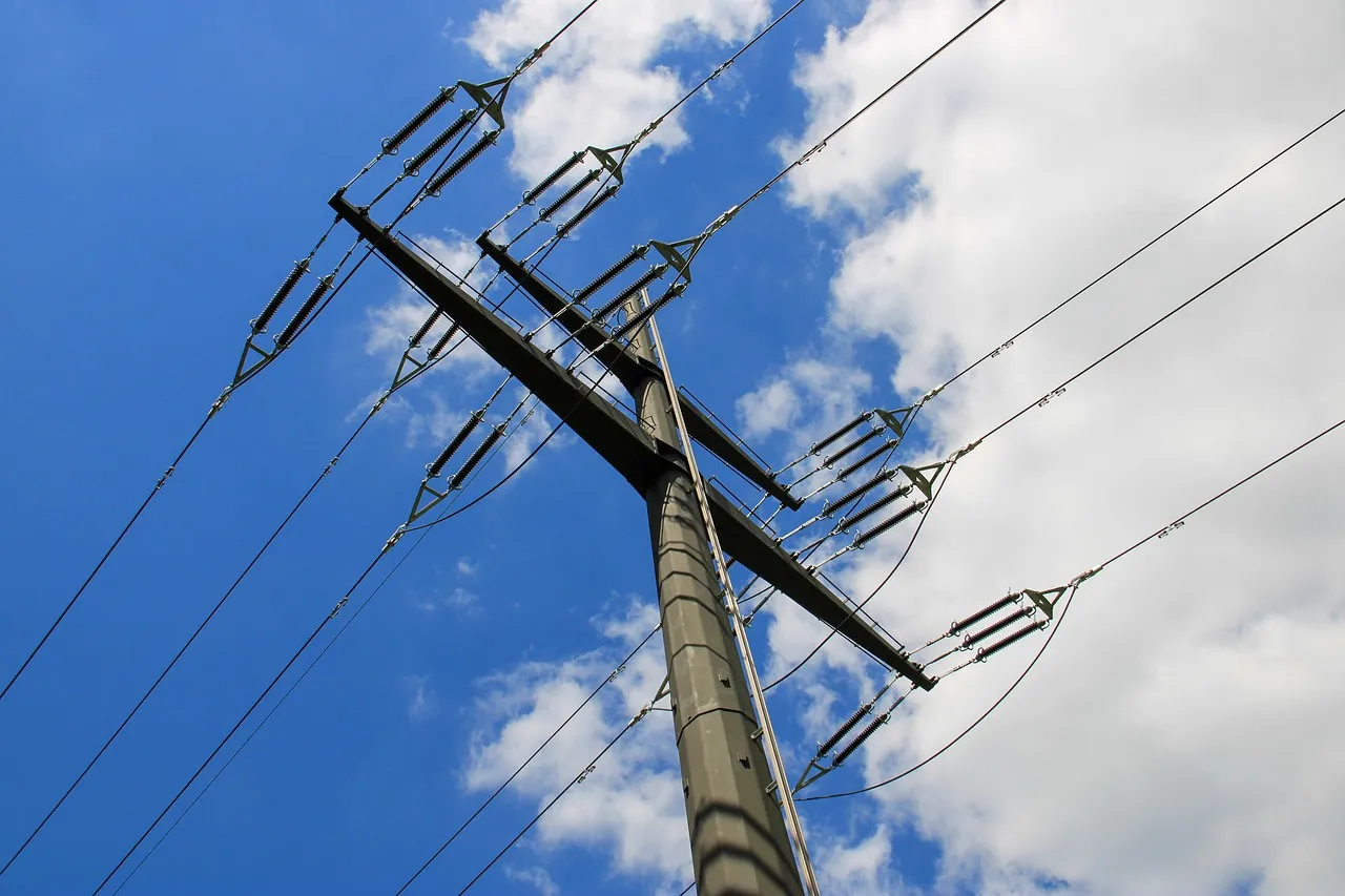 A concrete power pole carrying high-voltage overhead lines on ceramic insulators against a blue sky.