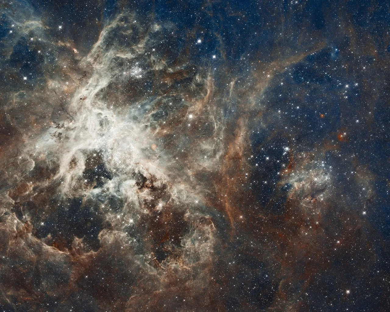 A dense star-forming region photographed against deep space, with filaments of red and blue gas threaded through thousands of resolved stars