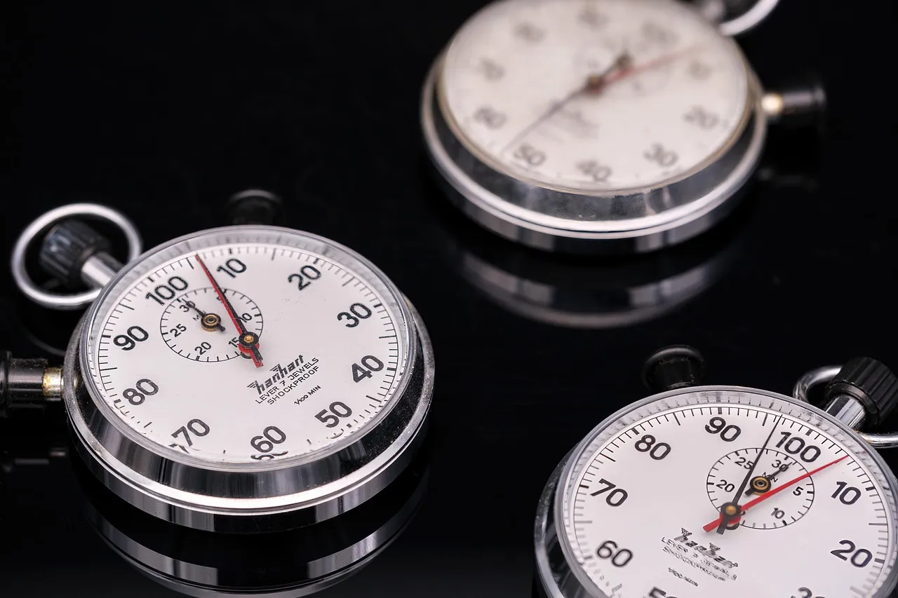 Three mechanical stopwatches on a reflective black surface, each stopped at a different reading on its dial
