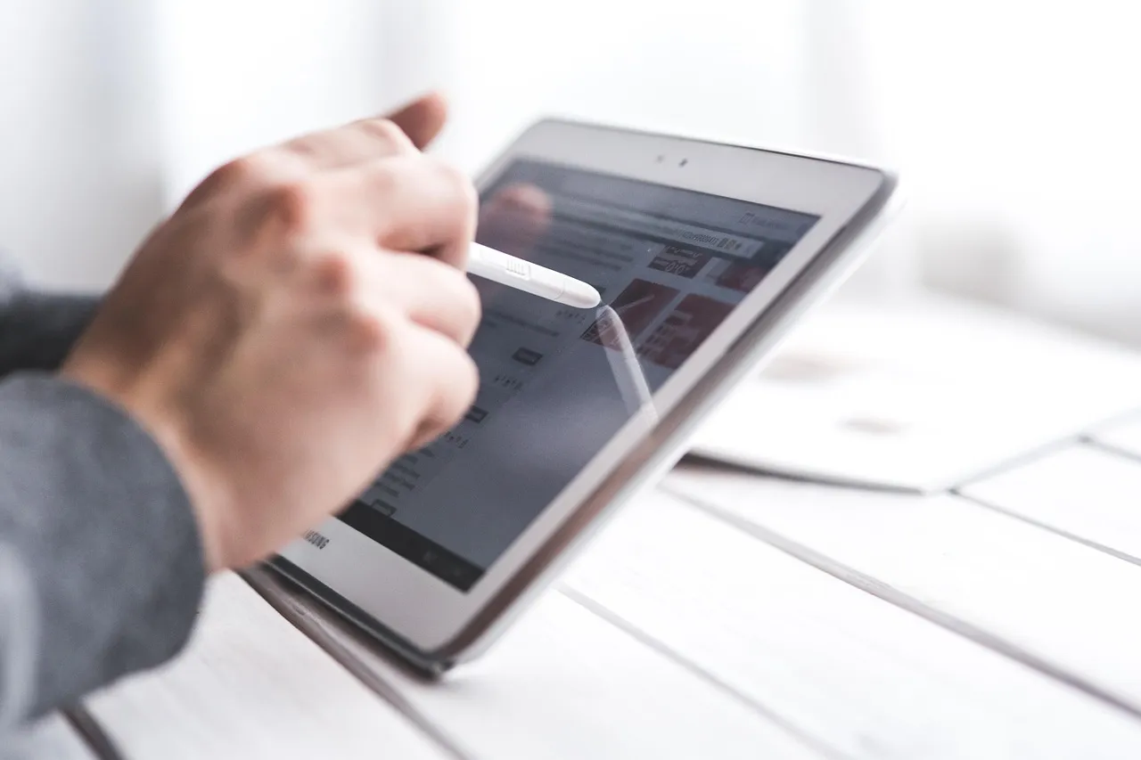 A hand using a stylus on a tablet screen
