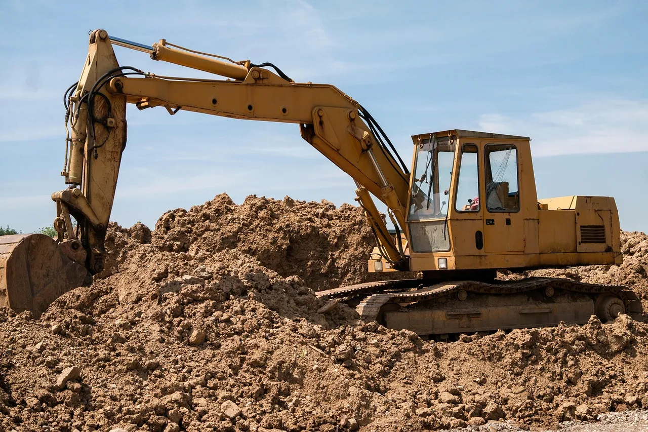 A yellow tracked excavator standing on a mound of bare churned earth at a cleared construction site