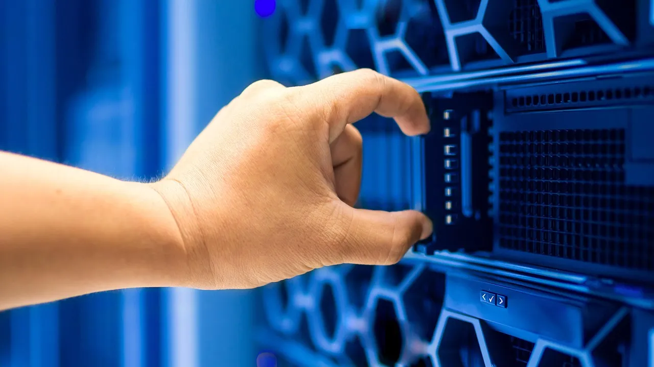 Hand pulling a blade server from a blue-lit rack, illustrating the evaluation infrastructure that failed to contain.