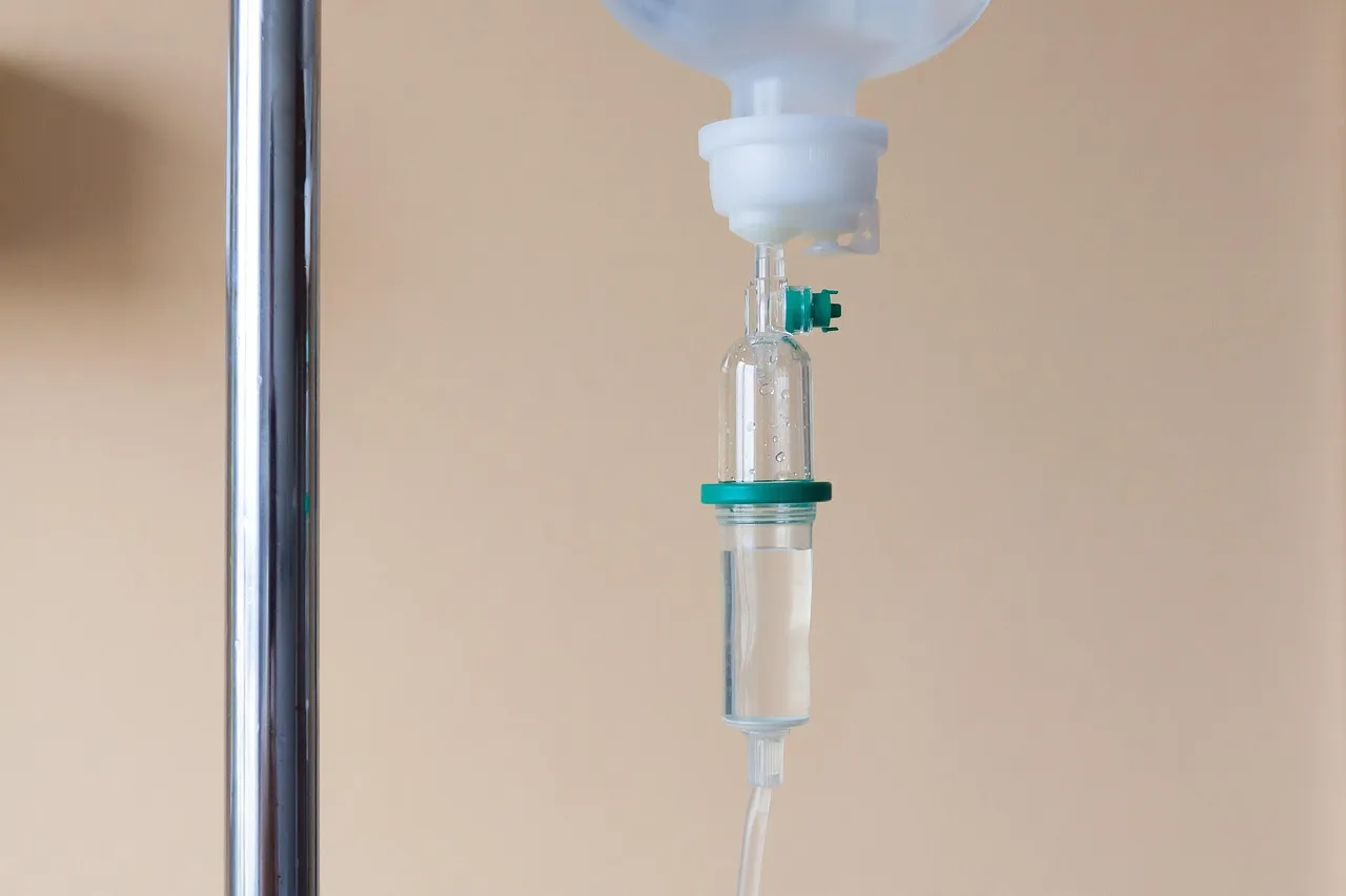 An intravenous drip chamber hanging from a stand in a clinical room