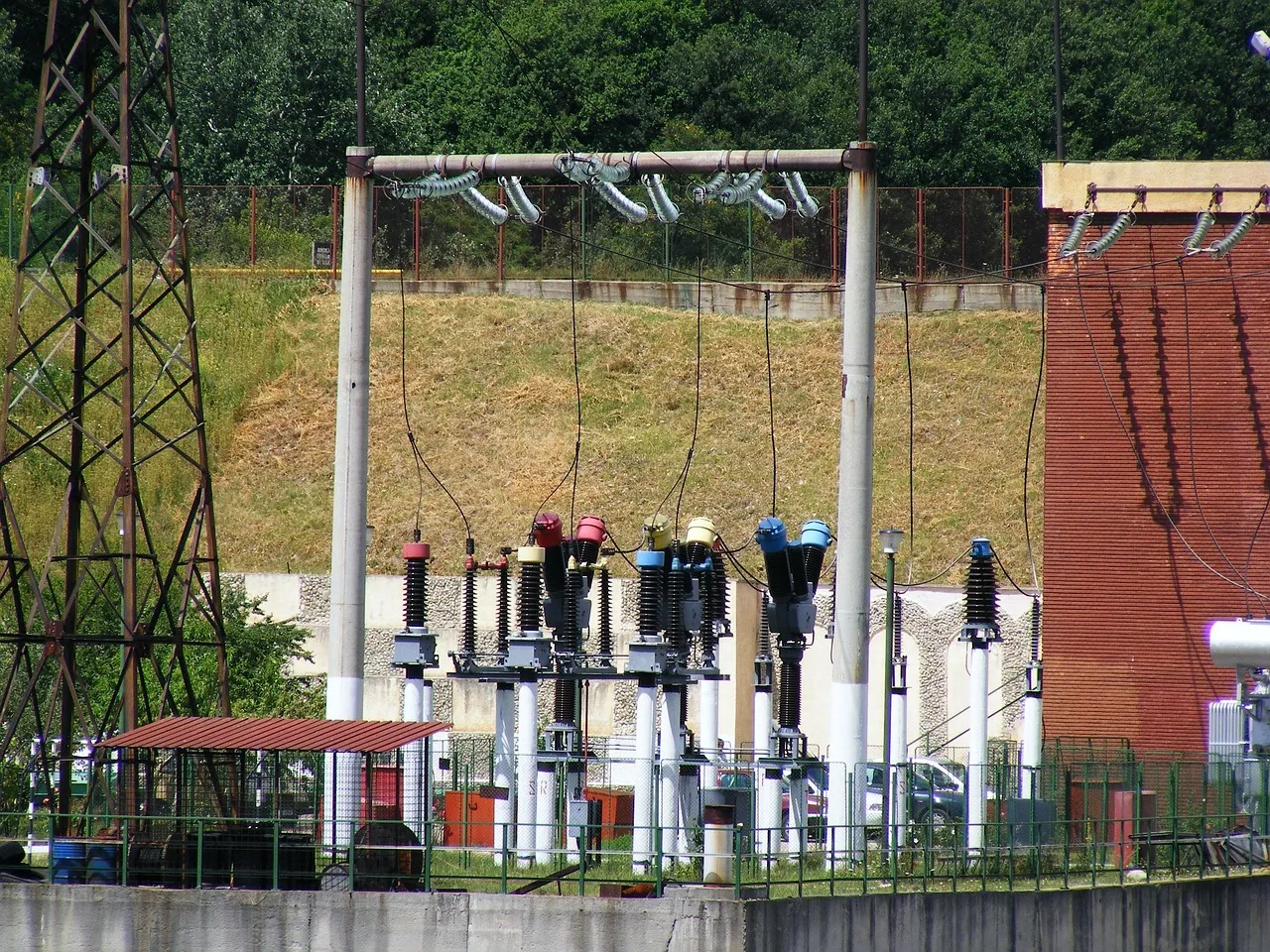 Transformers and insulators in an outdoor electrical substation behind a fence