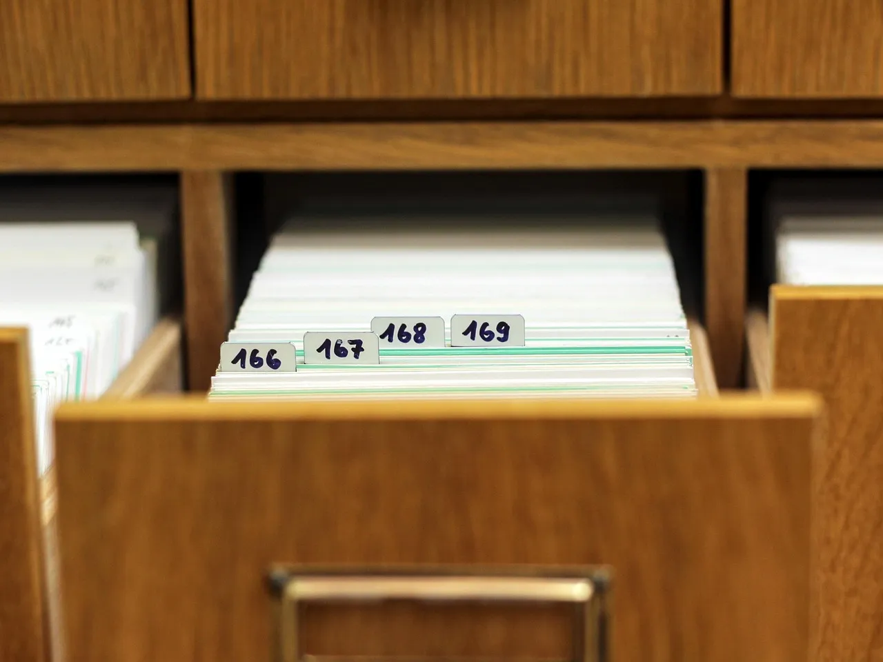 An open wooden card-index drawer pulled out of a cabinet, filled with upright paper cards behind numbered tab dividers reading 166, 167, 168 and 169.