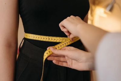Close-up of tailor's hands measuring a person's waist with a yellow tape.