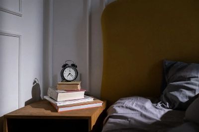 A cozy bedroom setting with books and an alarm clock on a nightstand next to a bed.